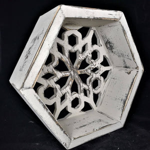 A white distressed wood hexagon shelf with a pierced back that looks similar to a snowflake design. It has 3.5" room inside of the shelf to put a small plant or picture frame